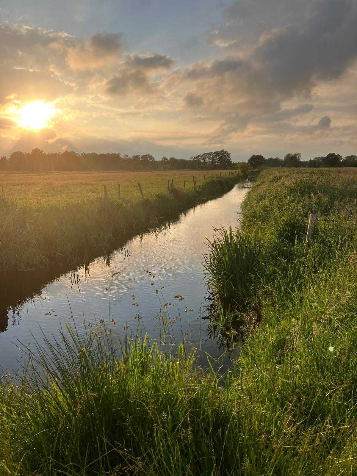 Zonsondergang met een polder en sloot op de voorgrond.