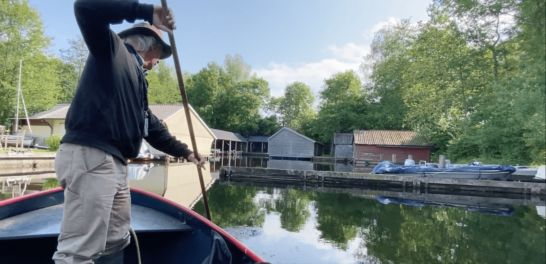Man staat in een bootje en met een lange stok wijst hij het water in. 