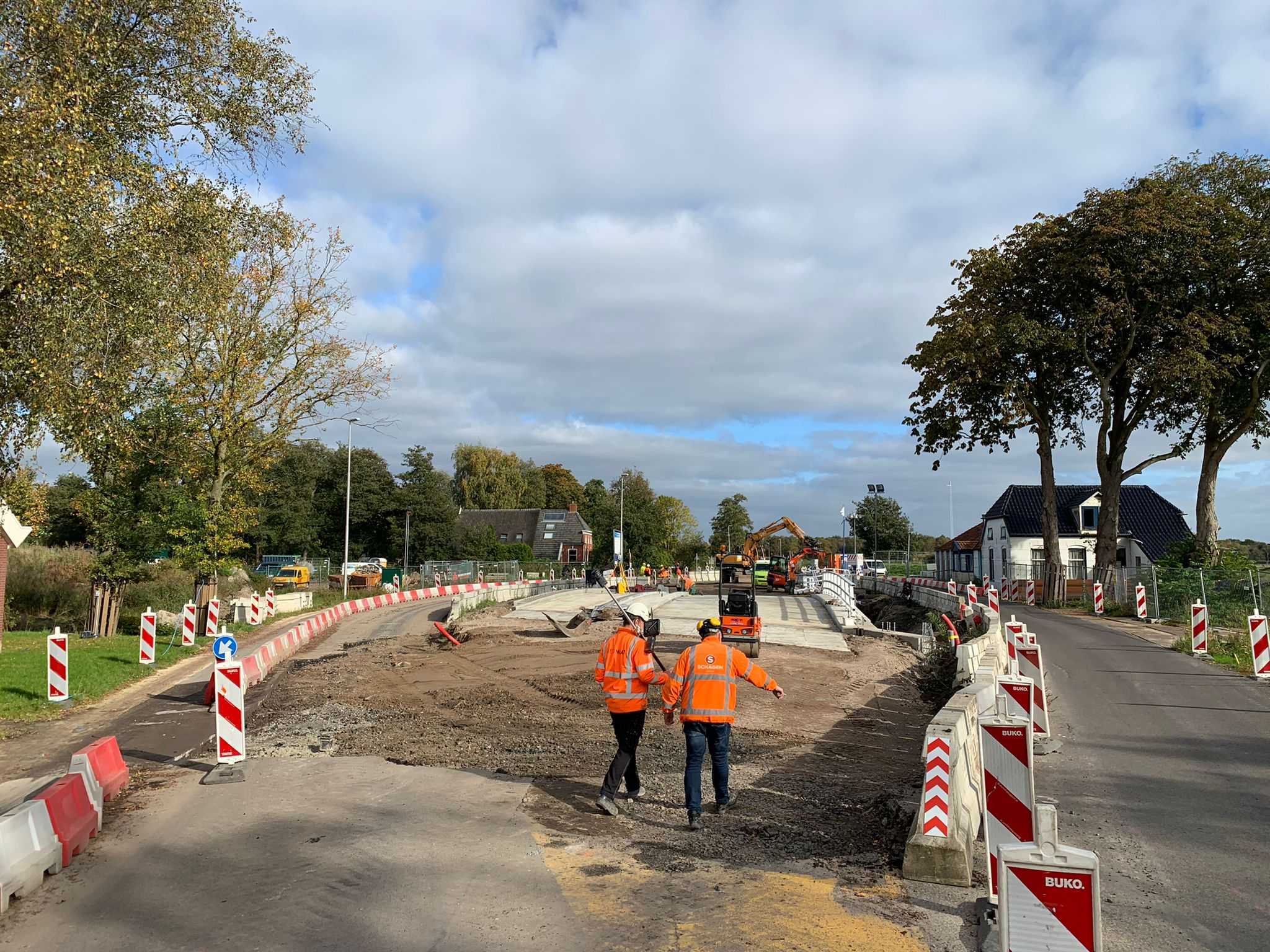 Bouwplaats met twee medewerkers in oranje jassen.