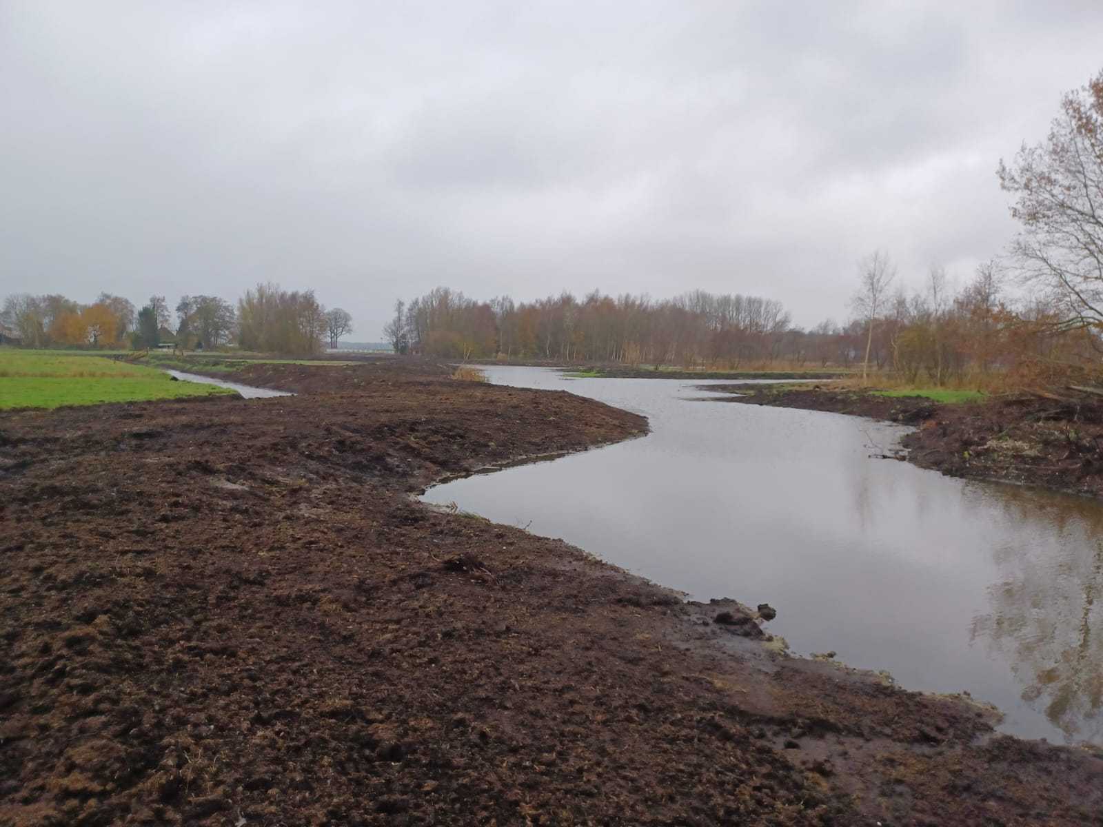 Slenk tussen twee kades, met bomen en gras in de achtergrond.