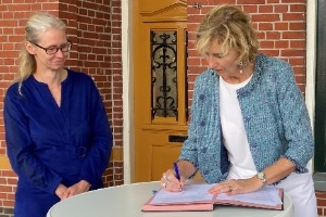 Twee vrouwen ondertekenen een overeenkomst aan een hoge tafel.