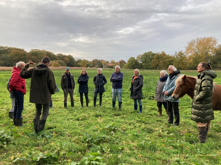 Meerdere mensen staan in een halve cirkel in een grasveld. Rechts in beeld staat een pony.
